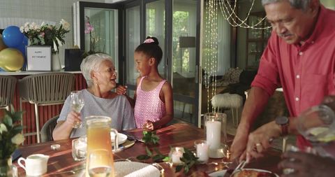 Multigenerational Family Celebrating Retirement Around Sunlit Dining Table With Candles