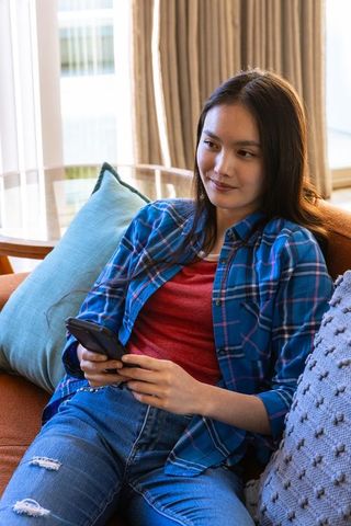 Asian Woman Using Smartphone Relaxing on Sofa in Modern Living Room