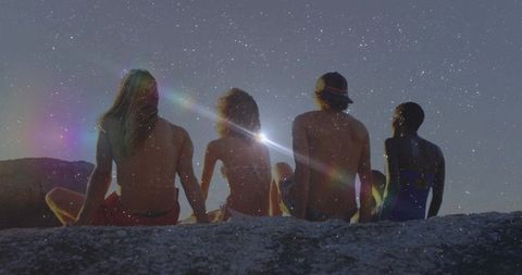 Friends Stargazing on Rocky Ledge Under Night Sky