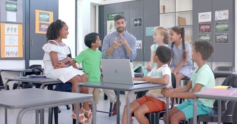 Engaging teacher leading elementary students around laptop in bright modern classroom