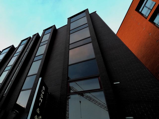 Photograph of a modern office building with a glass facade and brickwork, set against a slightly blue sky. Capture highlights the sleek design and reflective quality of the glass windows. Suitable for use in articles or promotions related to architecture, urban development, commercial real estate, corporate branding, or modern workplaces.
