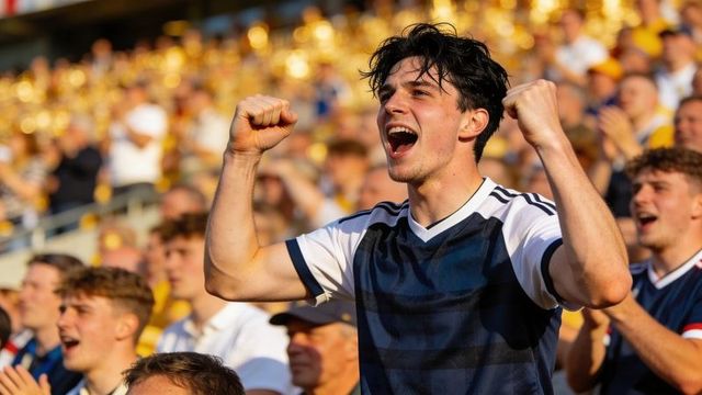 Triumphant young fan cheering with raised fists in packed stadium at golden hour