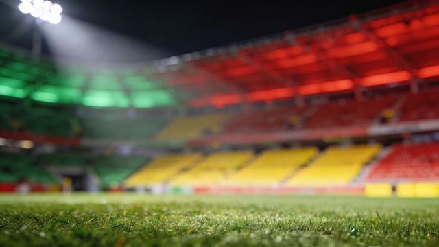 Close-up football pitch grass gleaming under floodlights with green yellow red stands