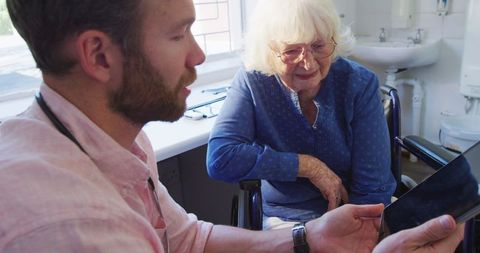 Doctor Consulting Senior Patient Using Tablet in Retirement Home