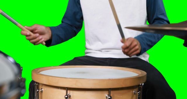 Mid section of drumer playing drum against green screen