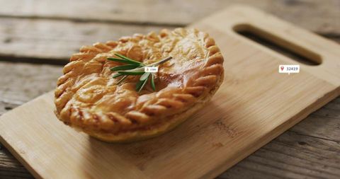 Golden braided savory pie topped with rosemary sprig on wooden cutting board closeup warm