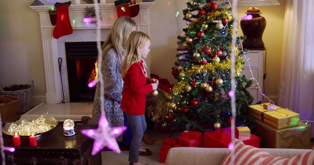 Caucasian woman and girl decorate a Christmas tree at home. They share a festive moment surrounded by holiday decorations and gifts.