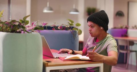 Young man working in modern coworking booth with laptop and notebook, focused productivity