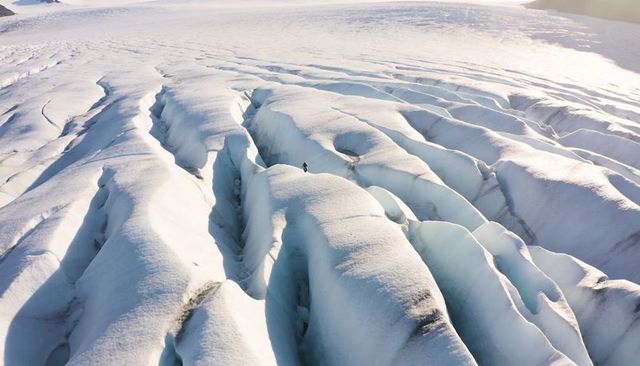 Solo explorer standing on glacier ridge surveying deep crevasses and expansive icefield