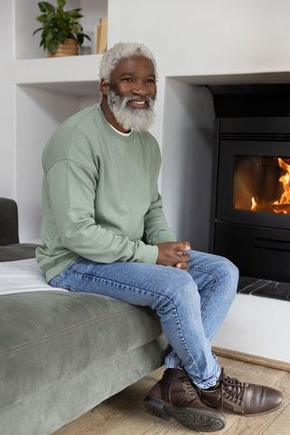 Senior african american man sitting on sofa smiling by fireplace in cozy home interior