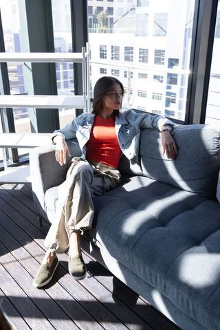 Relaxing on sunlit high-rise sofa woman wearing denim jacket in modern city loft
