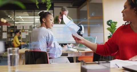 Coworkers exchanging documents with digital overlay in modern open office collaboration