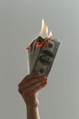 Hand Holding Burning Dollar Bills Signifying Financial Waste