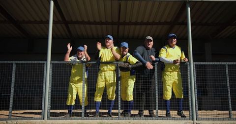 Baseball teammates cheering from dugout wearing yellow uniforms and blue caps
