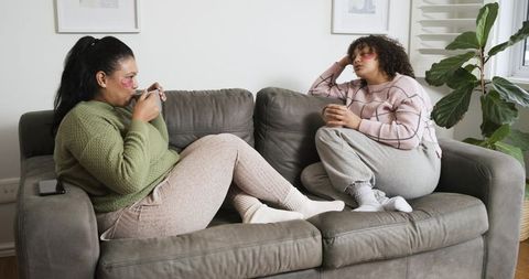 Friends sharing cozy conversation on gray sofa holding mugs in bright minimalist living room