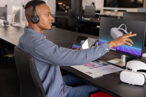 African American professional testing VR headset, pointing at monitor while using tablet