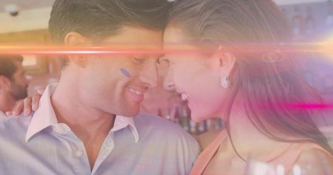 Romantic couple leaning foreheads smiling in lounge with colorful light leaks and cocktails