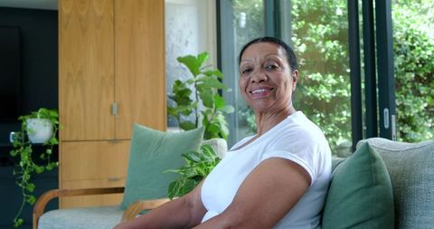 Senior african american woman smiling on cozy living room sofa with sunlit plants