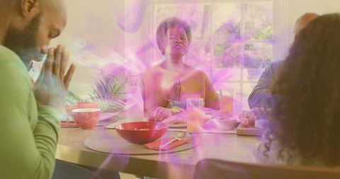 Multigenerational family praying together at breakfast table, woman leading blessing