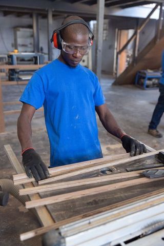 African American Carpenter Working with Wooden Strips Wearing Safety Goggles and Ear Muffs