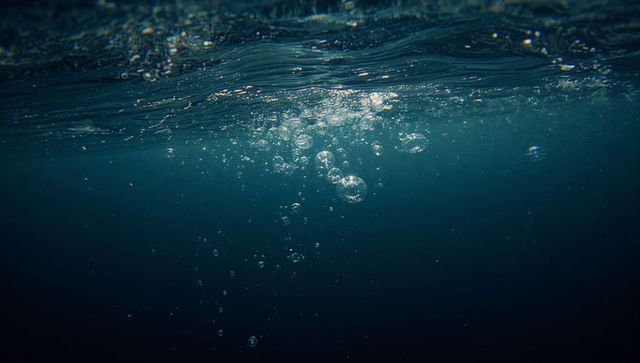 Rising bubbles beneath rippled ocean surface with sunbeams, particles and deep blue mood