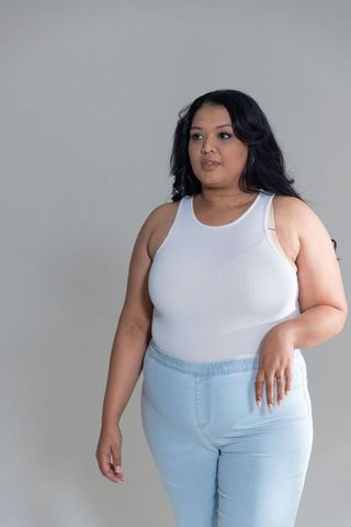 Curvy woman standing wearing white ribbed tank and light jeans showing ring and necklace