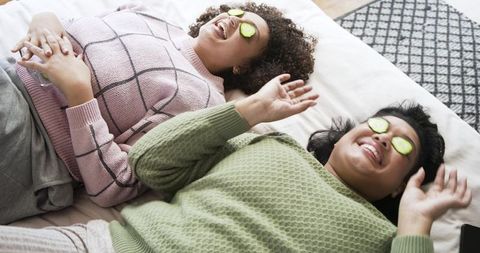 African american friends relaxing with cucumber eye masks on bed cozy home spa moment