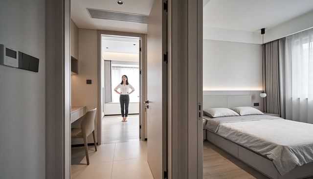 Barefoot woman standing in modern minimalist apartment hallway surveying bright bedroom interior