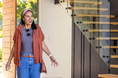 Mature woman discovering modern home with glass staircase, open pivot door, casual style