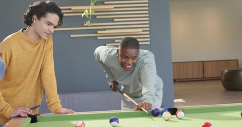 Young men playing pool in modern lounge aiming precision shot for friendly competition