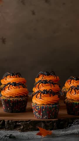 Vertical panning over Halloween cupcakes with spider toppers, flickering candle reveal