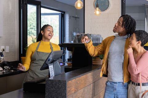 Friendly barista greeting smiling couple at modern cafe counter with pos terminal and warm lighting