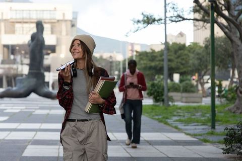 Young woman walking on campus holding notebooks and talking on smartphone