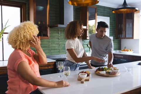 Diverse friends gathering at kitchen island choosing charcuterie board with wine and fruit