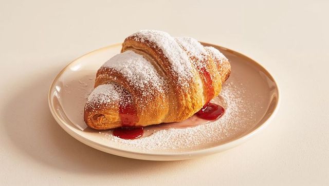 Buttery croissant sitting on beige plate dusting powdered sugar and raspberry jam drizzle
