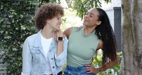 Two african women laughing and smiling in backyard wearing smartwatches and denim