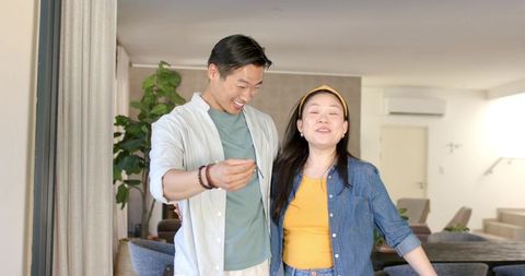 Young asian couple celebrating new home, man holding key by sunlit living room window