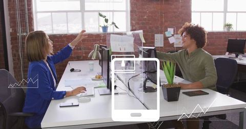 Colleagues collaborating across plexiglass divider in bright urban open office