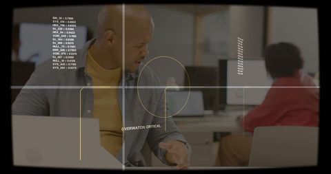 Bald professional turning and reaching at open-plan office desk with hud overlay and laptop