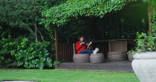 Senior caucasian woman relaxing in garden, sitting with feet up, drinking coffee and reading book. retirement lifestyle at home alone.