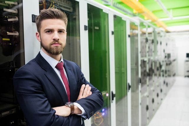 Technician standing confidently with arms crossed in a server room, surrounded by server racks and IT infrastructure. Ideal for use in technology, IT services, cybersecurity, data management, and professional business contexts.