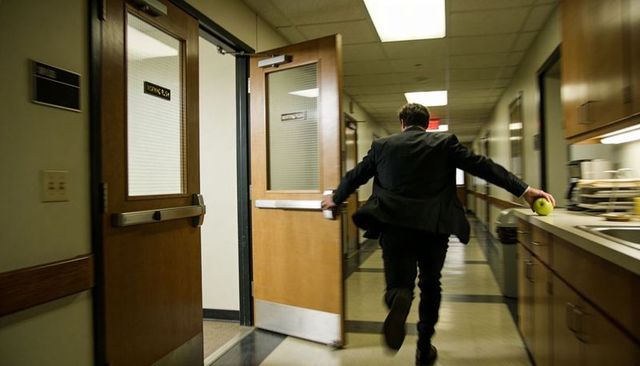 Executive walking briskly down medical office corridor holding tennis ball while opening door