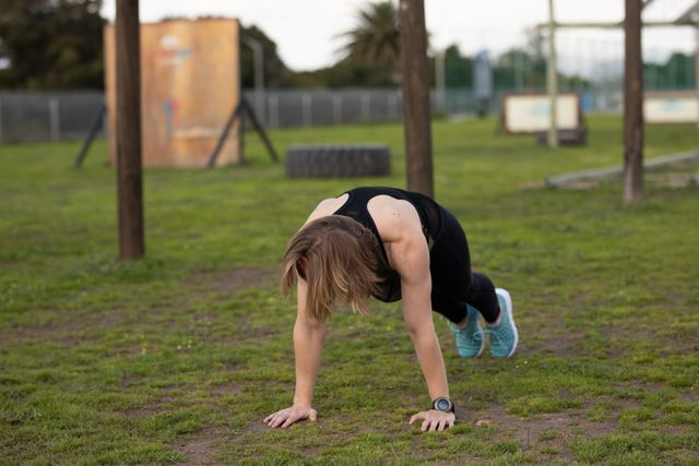 Front view of a Caucasian woman wearing sports clothes doing press ups on the grass at an outdoor gym during a bootcamp training session