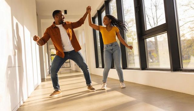 Sunlit couple dancing in modern corridor holding hands and laughing