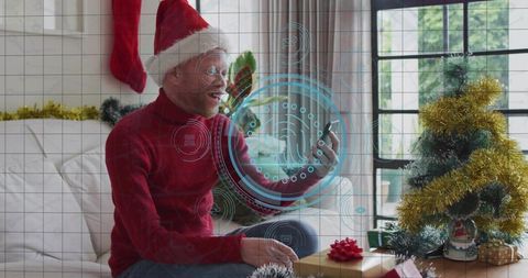 Man wearing santa hat using smartphone with holographic ar interface beside christmas tree