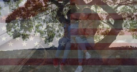 Two women sitting on stone wall under tree with american flag double exposure