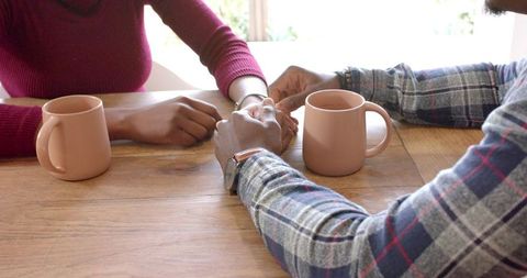 Couple Holding Hands in Café on Wooden Table