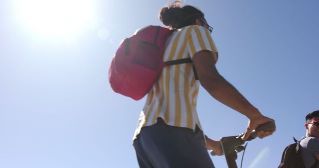 Young person with backpack riding scooter under bright sun - Download Free Stock Images Pikwizard.com