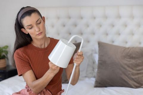 Woman assembling minimalist white table lamp on bed in cozy neutral bedroom interior