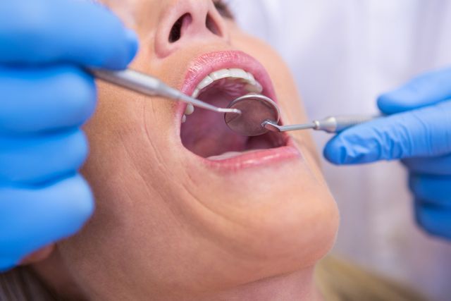 This image shows a dentist examining a patient's teeth using dental tools. The close-up view highlights the dental mirror and probe, emphasizing the importance of oral health and regular dental checkups. This image can be used for articles, blogs, or advertisements related to dental care, oral hygiene, healthcare services, and dental clinics.